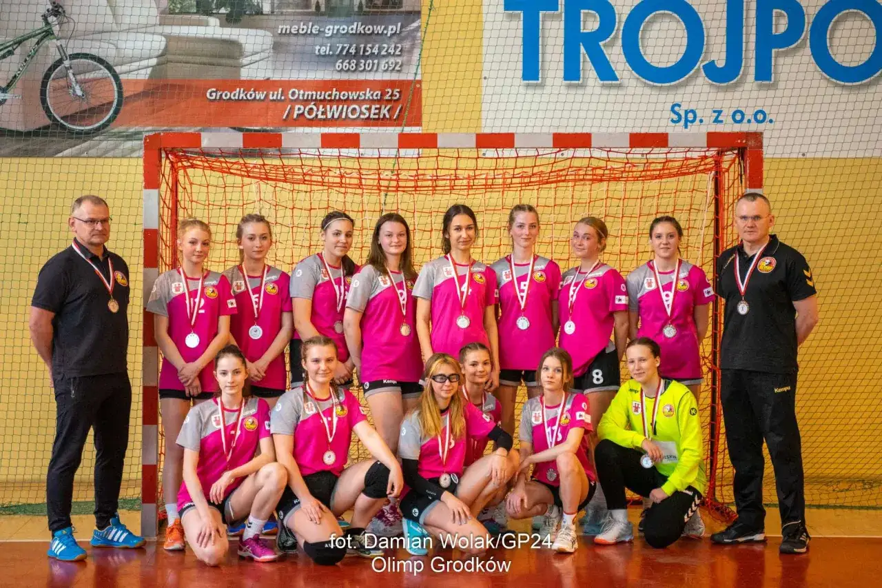 Drużyna piłki ręcznej Olimp Grodk&oacute;w z trenerem i medalami po zwycięstwie.
