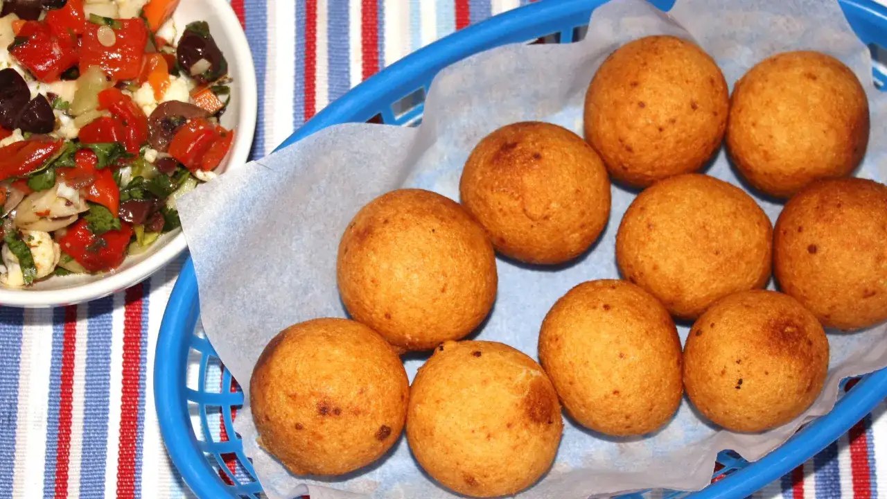 En korg med gyllene friterade bollar, som visar c&oacute;mo hacer bu&ntilde;uelos. Bredvid en sk&aring;l med en f&auml;rgglad sallad.
