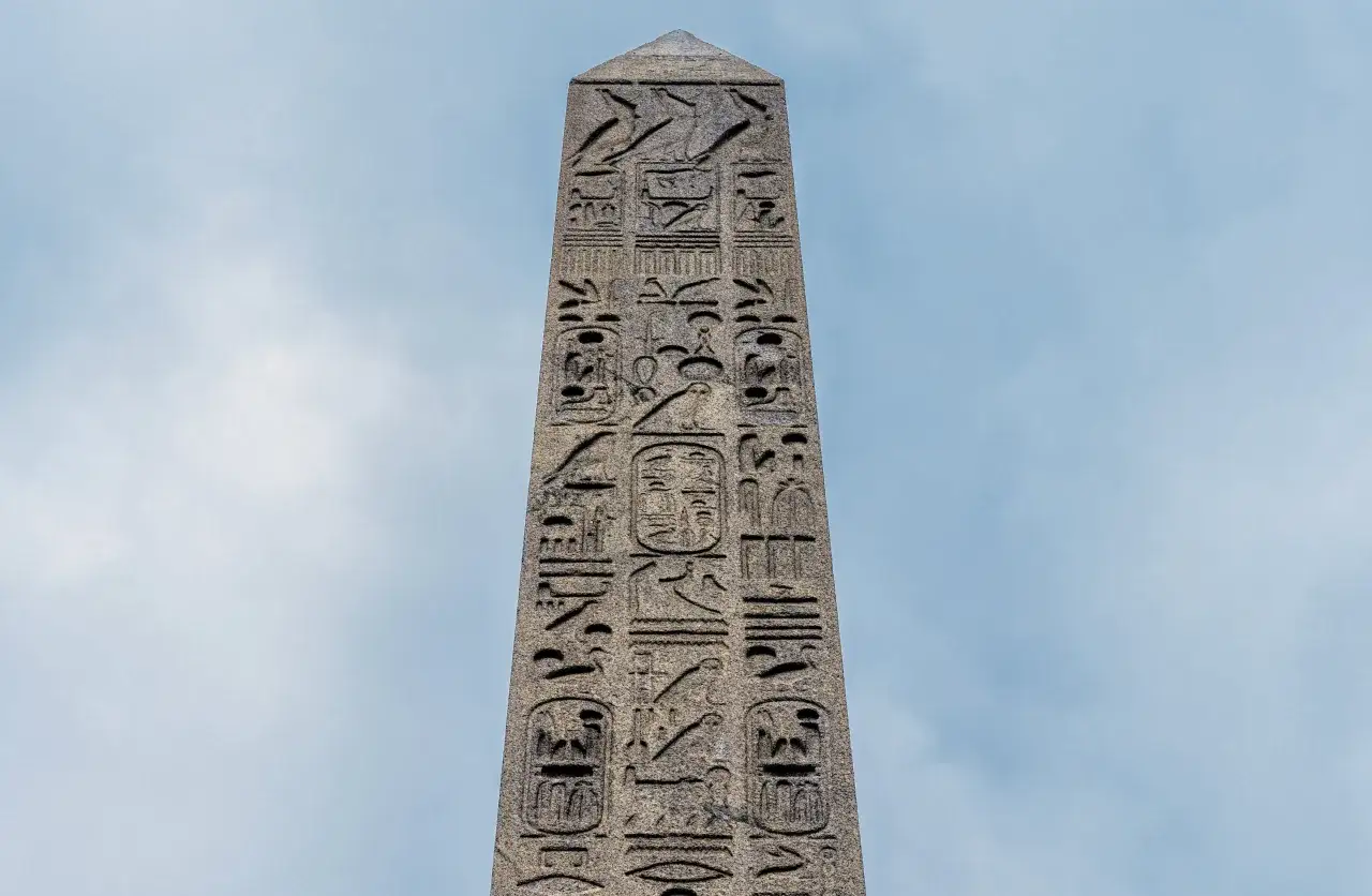 En stenobelisk med hieroglyfer, möjligen Kleopatras nål, reser sig mot en molnig himmel.