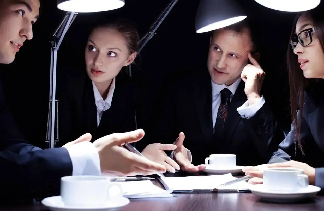 Cuatro personas en trajes negros participan en entrevistas a emprendedores, bajo la luz de lámparas de escritorio.