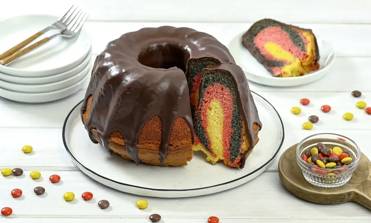 Bunter Marmorkuchen mit Schokoladenglasur, inspiriert von deutschen Kuchen Rezepten. Ein St&uuml;ck ist angeschnitten und zeigt die Farben Schwarz, Rot und Gelb.