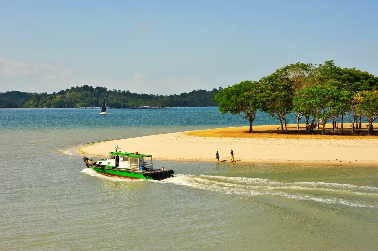 Grüne Fähre fährt am **Singapur Strand** vorbei. Im Hintergrund eine Segelyacht und bewaldete Hügel.