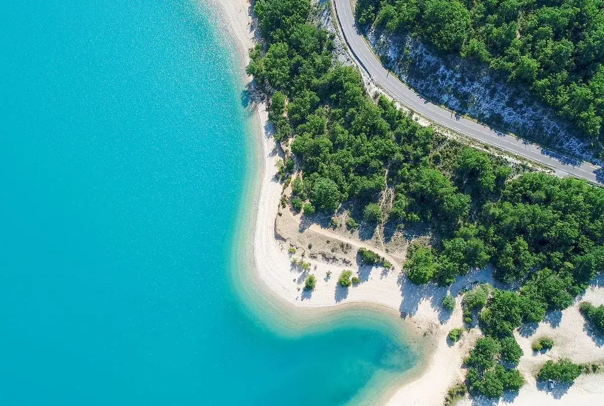 Vue aérienne d'un lac aux eaux turquoise, bordé d'une plage de sable clair et d'une forêt dense. Un endroit parfait pour la baignade.