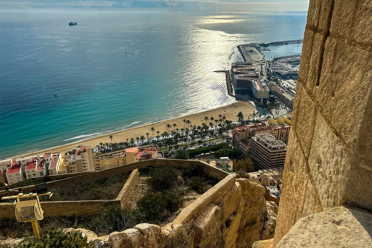 Widok z zamku na plażę i port w Alicante. Słoneczna plaża, turkusowe morze i miejska zabudowa to jedne z wielu **Alicante atrakcje**.