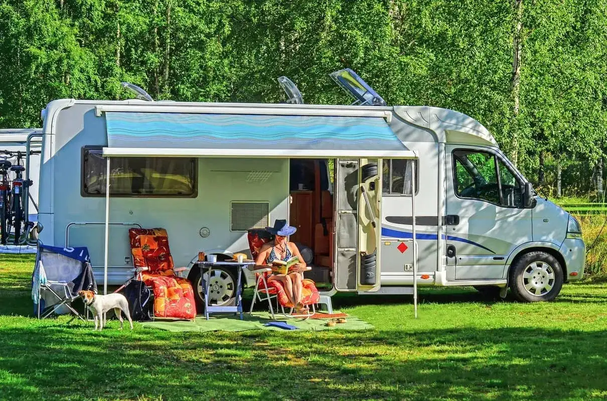 Frau liest unter der ausgefahrenen Wohnmobil Markise, während ein Hund auf dem Rasen steht. Perfekt für die Wohnmobil Markise reinigen und entspannen.