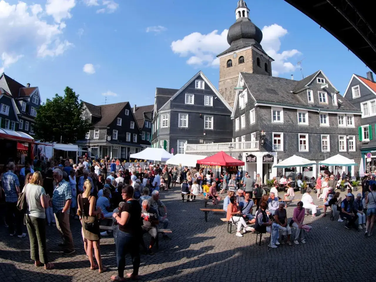 Buntes Treiben auf dem Markt Remscheid. Menschen genie&szlig;en das Sommerfest vor historischen Fachwerkh&auml;usern und dem Kirchturm.