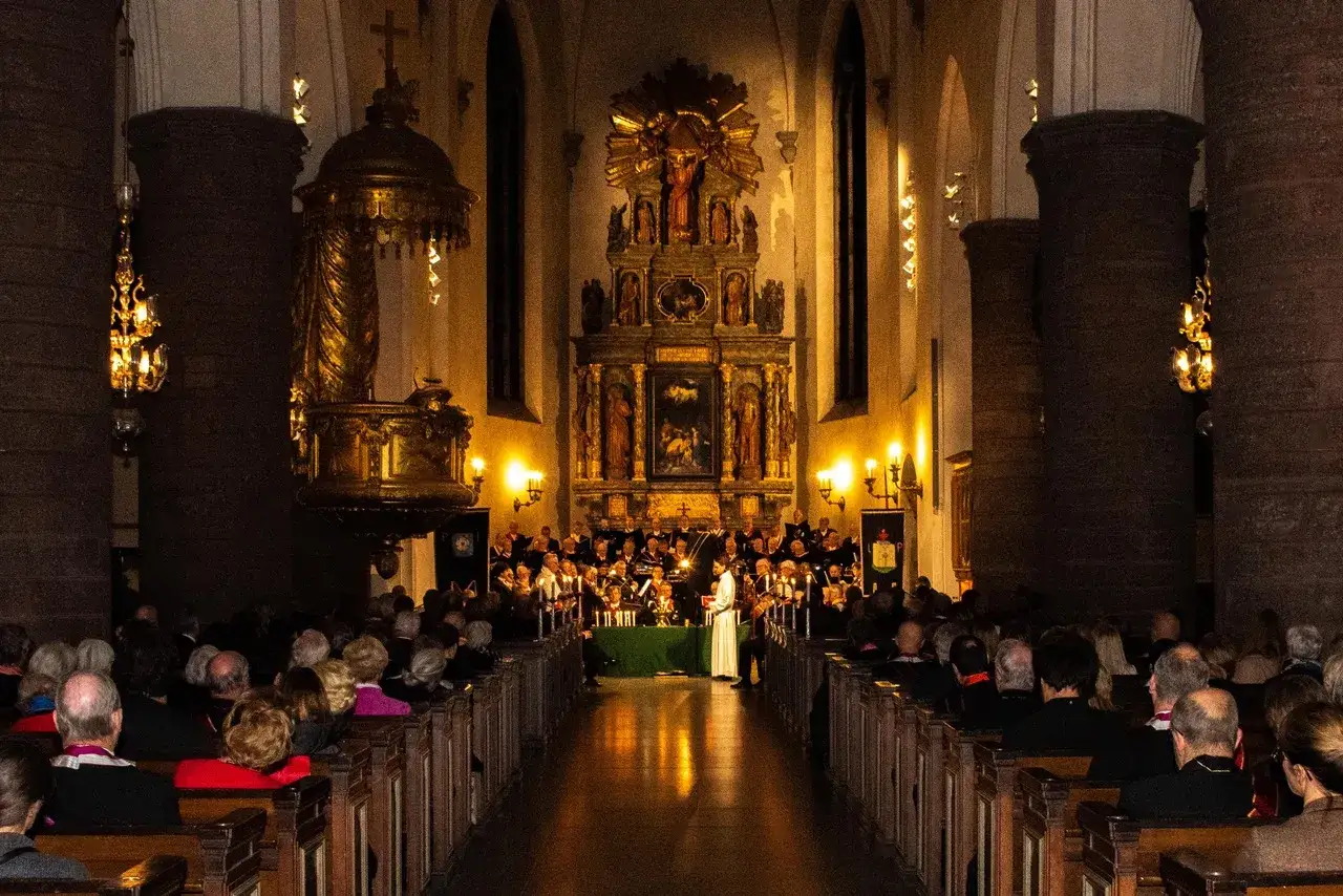 Publik lyssnar på en kör i St Jacobs kyrka. En imponerande altartavla lyser upp bakgrunden.