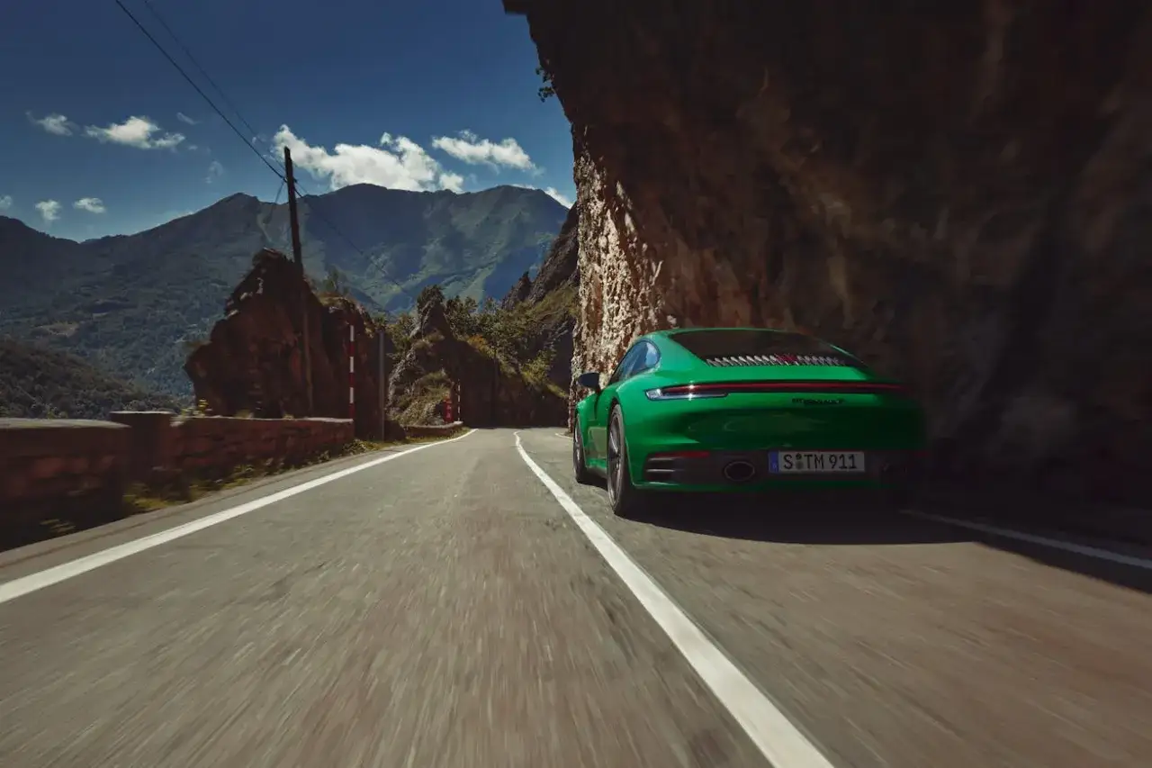 Zielony Porsche Carrera mknie krętą górską drogą, otoczony skalistymi zboczami i bujną zielenią.