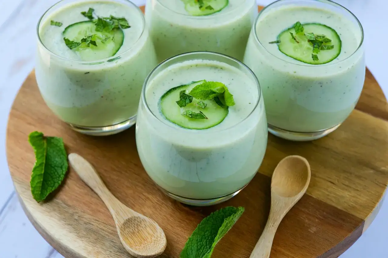 Quatre verres de gaspacho concombre frais, d&eacute;cor&eacute;s d'une rondelle de concombre et de feuilles de menthe. Deux petites cuill&egrave;res en bois sont pos&eacute;es sur le plateau.