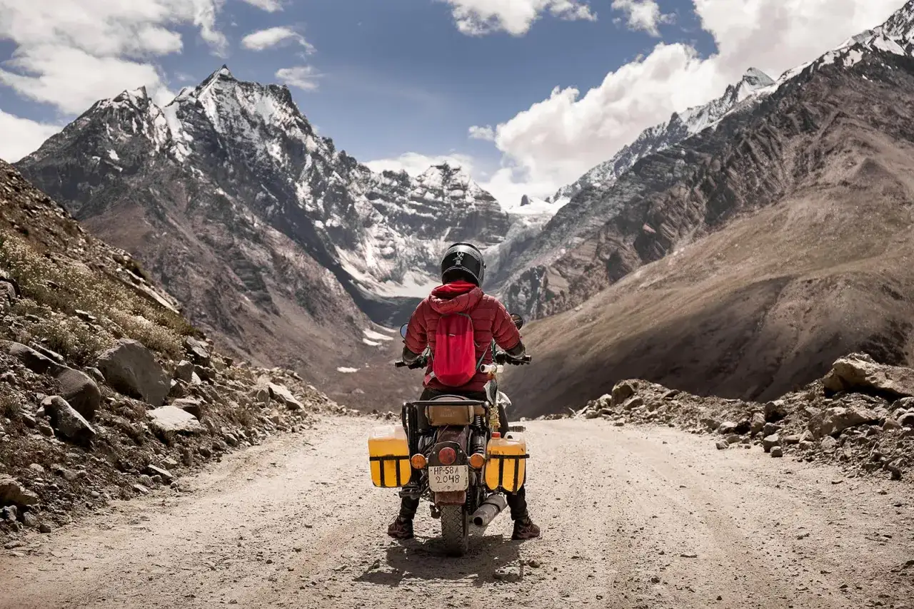 Motocyklista w czerwonej kurtce i kasku na tle majestatycznych gór w Indiach. Podróż do Leh Indie.