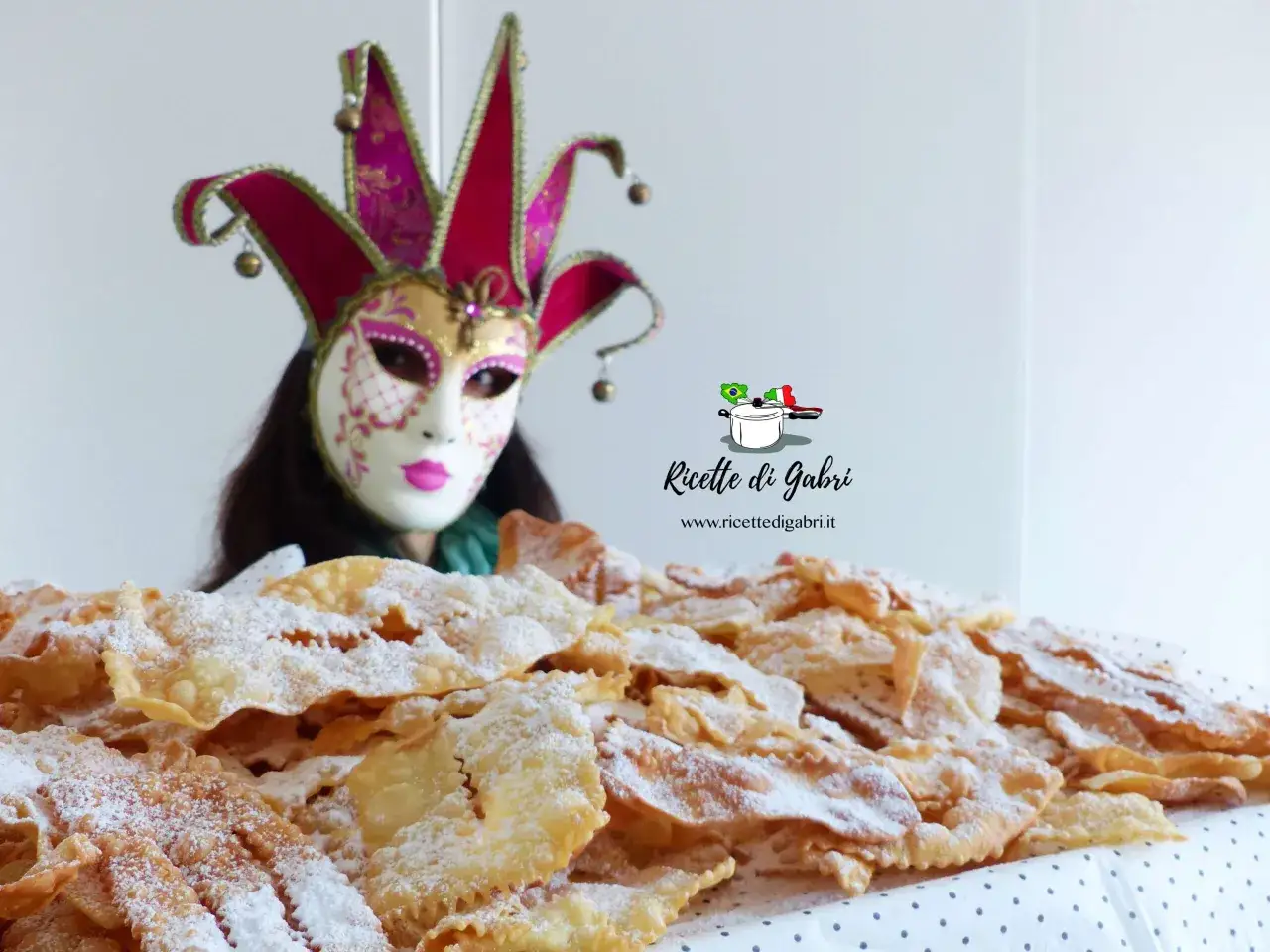 Maschera di carnevale e un mucchio di chiacchiere friabili e bollose, cosparse di zucchero a velo.