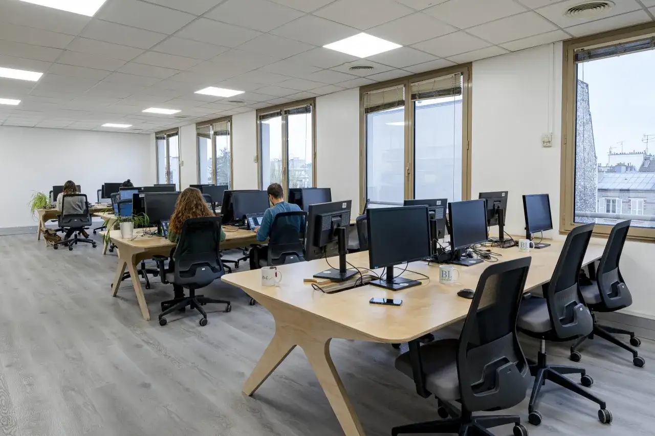 Bureau moderne avec plusieurs postes de travail. Le niveau sonore semble bas, respectant le code du travail pour un environnement propice &agrave; la concentration.