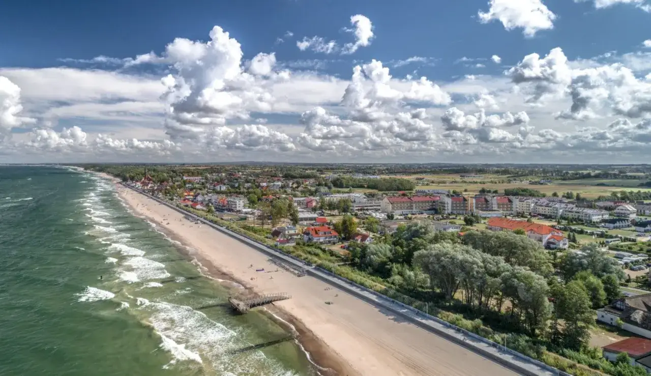 Szerokie plaże i promenady nad morzem, z zielenią i zabudową w tle.