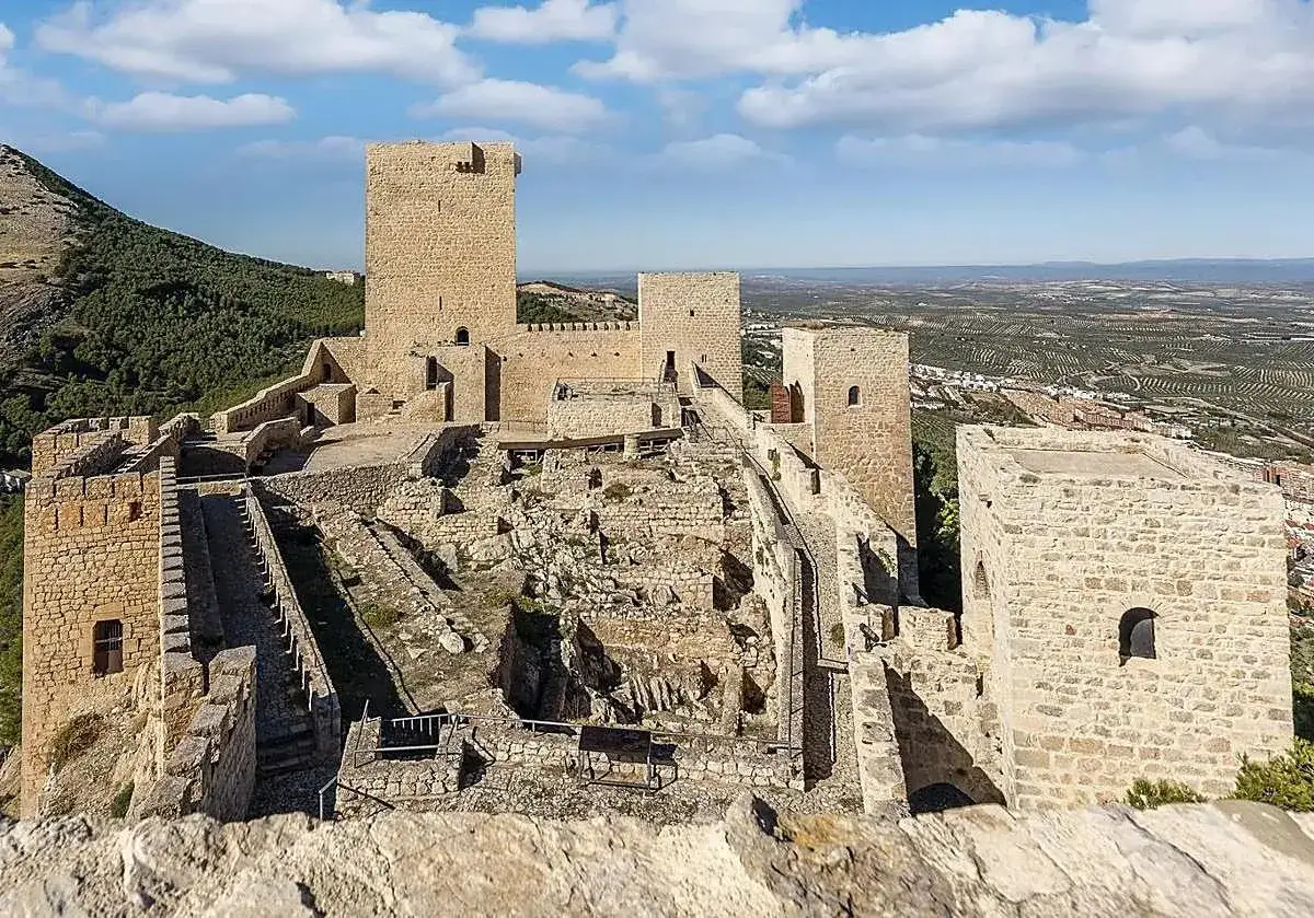 Castillo de Baños de la Encina, uno de los pueblos bonitos de Jaén, con sus imponentes torres y murallas de piedra bajo un cielo azul.