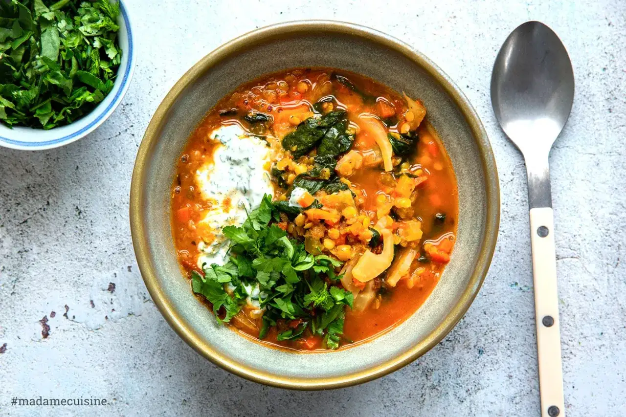 Herzhafte Linsen Rezepte: Eine Schüssel wärmender Linsensuppe mit Joghurt-Topping und frischer Petersilie, daneben eine kleine Schale gehackter Kräuter.