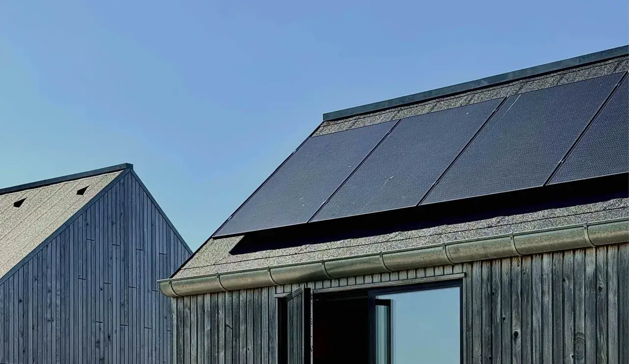Tak med monokristallina solceller och tr&auml;fasad mot bl&aring; himmel.