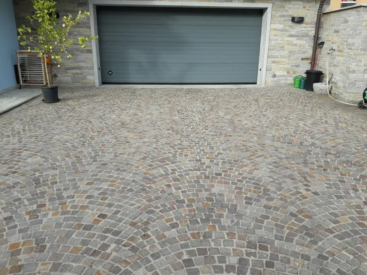 Un viale con una bellissima texture di sanpietrini disposti a ventaglio, che conduce a un garage moderno.
