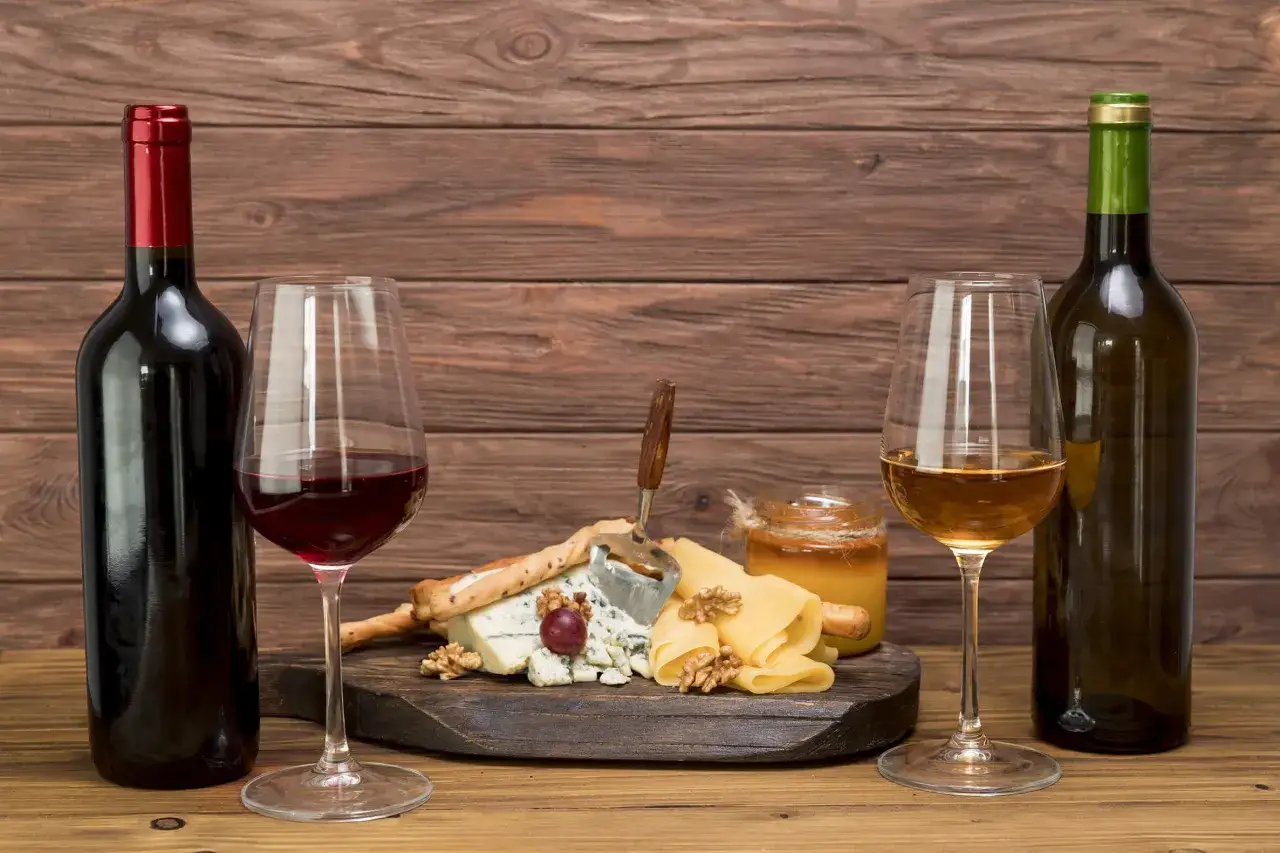 Bouteille de vin rouge et blanc, verres, plateau de fromages variés, noix, miel. Une invitation à découvrir quel vin rouge avec fromage.