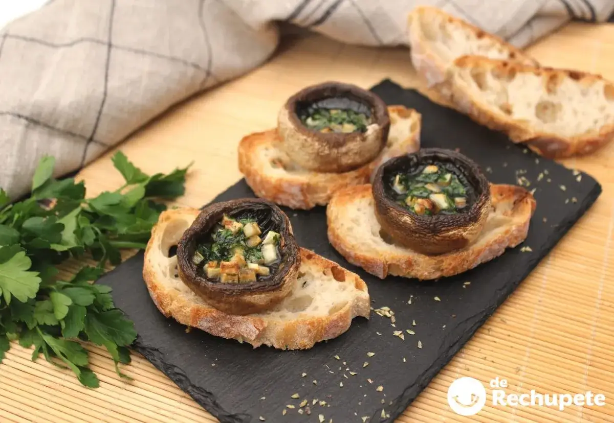 Champi&ntilde;ones al ajillo, rellenos y gratinados, servidos sobre rebanadas de pan r&uacute;stico. Un bocado delicioso.