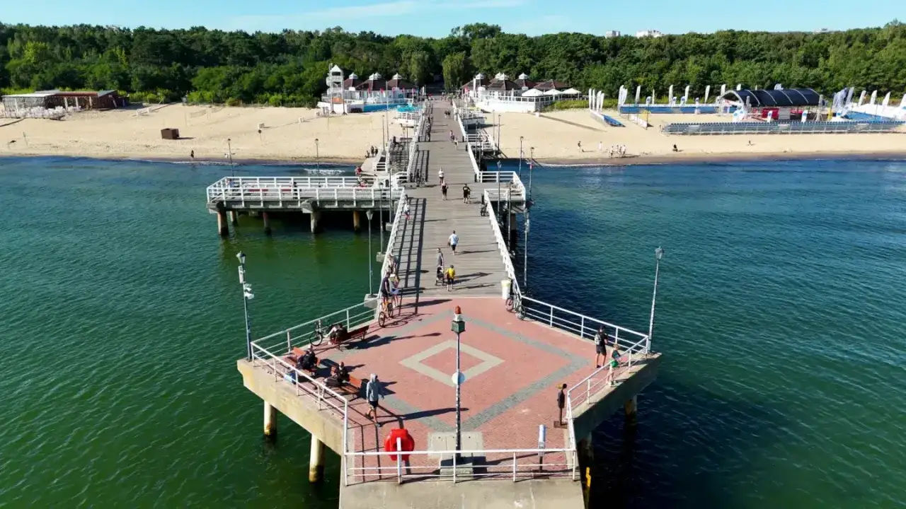 Molo w Gdańsku, gdzie widać, że jest morze. Ludzie spacerują i odpoczywają na plaży.