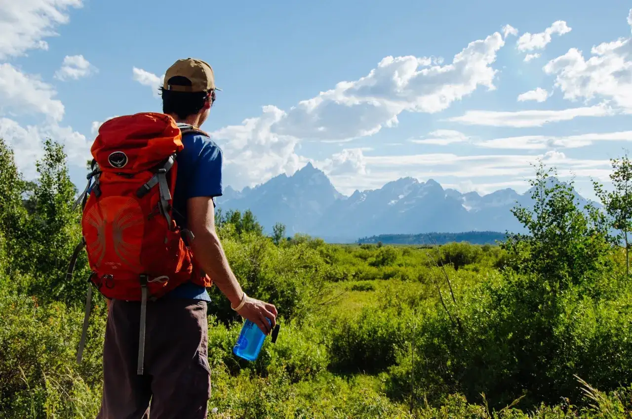 Mężczyzna z plecakiem podziwia g&oacute;ry. To właśnie jest hiking &ndash; przygoda na łonie natury.