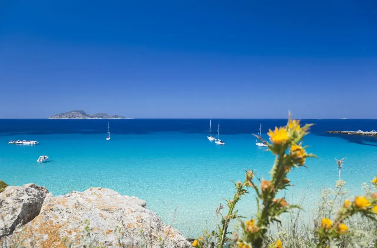 Splendida **Sicilia dove andare al mare**: acque cristalline, barche a vela e un'isola all'orizzonte.