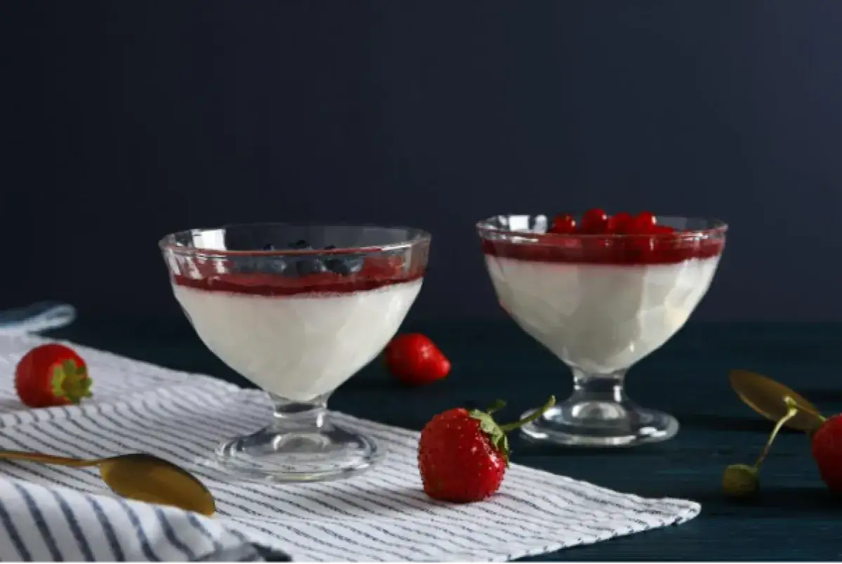 Dwie panna cotty: jedna na śmietance z jagodami, druga na jogurcie z malinami. Letni deser gotowy do degustacji.