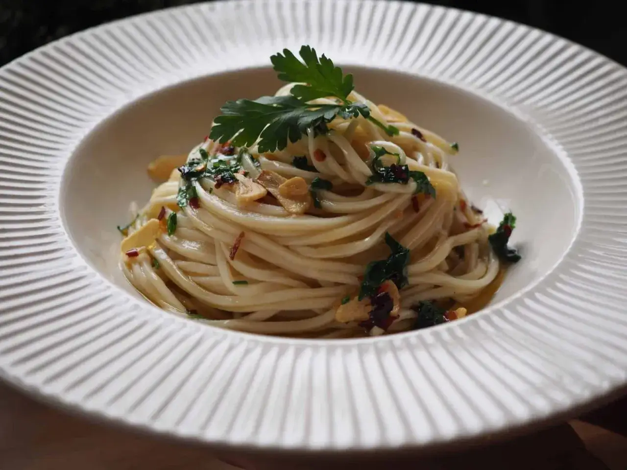 Pyszny, domowy makaron spaghetti z czosnkiem, chili i natką pietruszki, podany na białym talerzu.