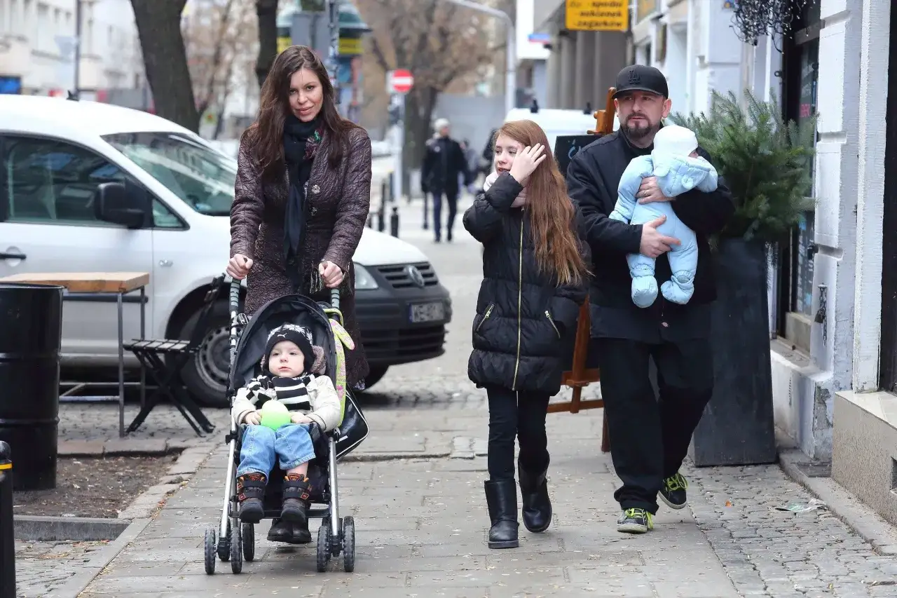 Rodzina spaceruje po mieście. Kobieta pcha wózek z dzieckiem, obok idzie dziewczynka i mężczyzna z niemowlakiem. Liroy dzieci.