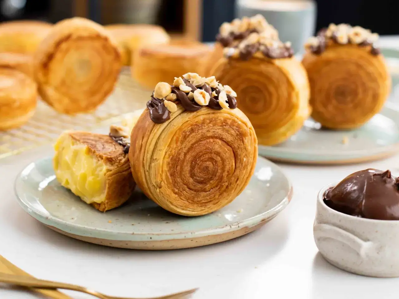 Deliciosos new york rolls con glaseado de chocolate y avellanas, uno abierto revela un cremoso relleno de crema pastelera.