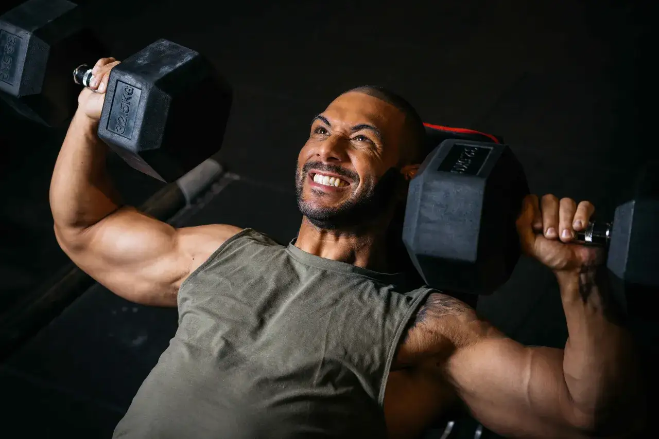Mann mit kr&auml;ftigen Armen hebt schwere Hanteln (32,5 kg) im **SST Training**. Sein Gesichtsausdruck zeigt pure Anstrengung und Entschlossenheit.