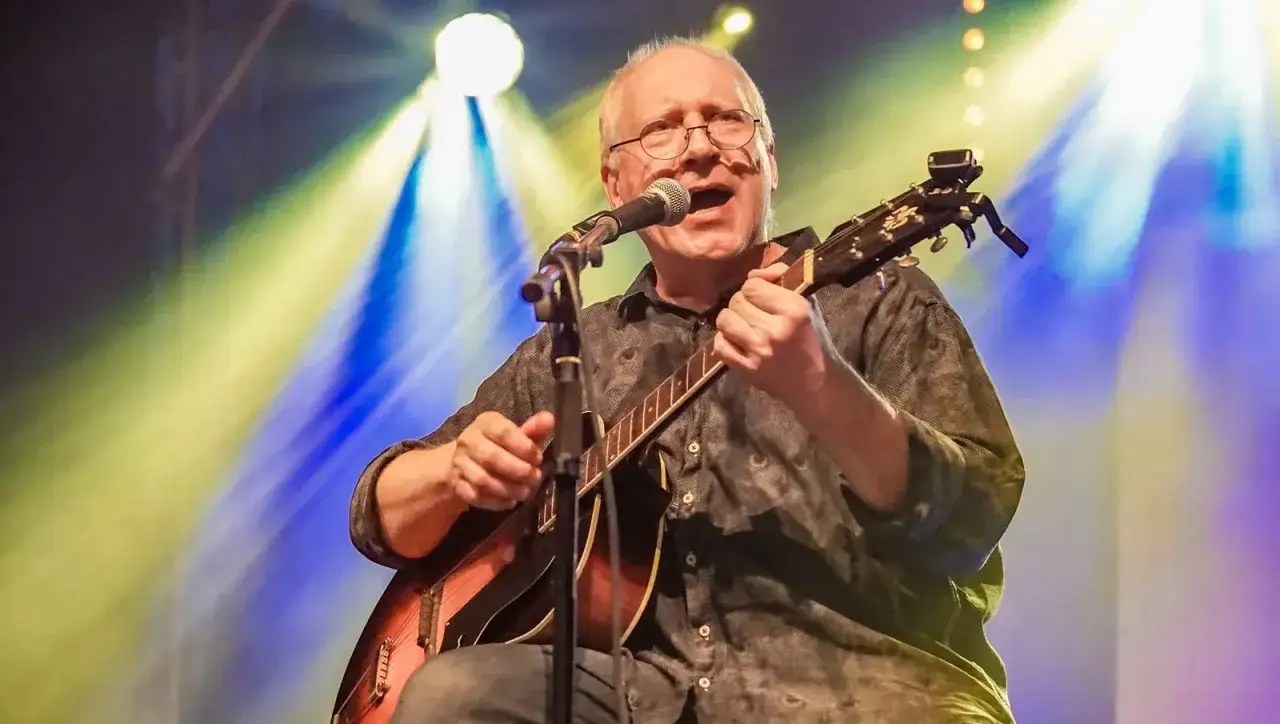 Kuba Sienkiewicz śpiewa i gra na gitarze akustycznej na scenie, oświetlony niebiesko-żółtymi światłami.
