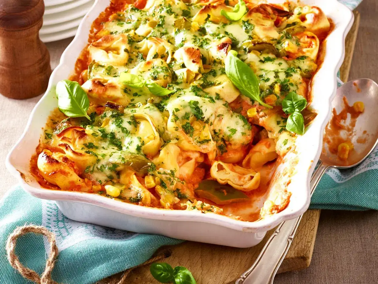 Herzhafter Tortellini-Auflauf mit geschmolzenem Käse, Mais und frischem Basilikum, serviert in einer weißen Auflaufform.