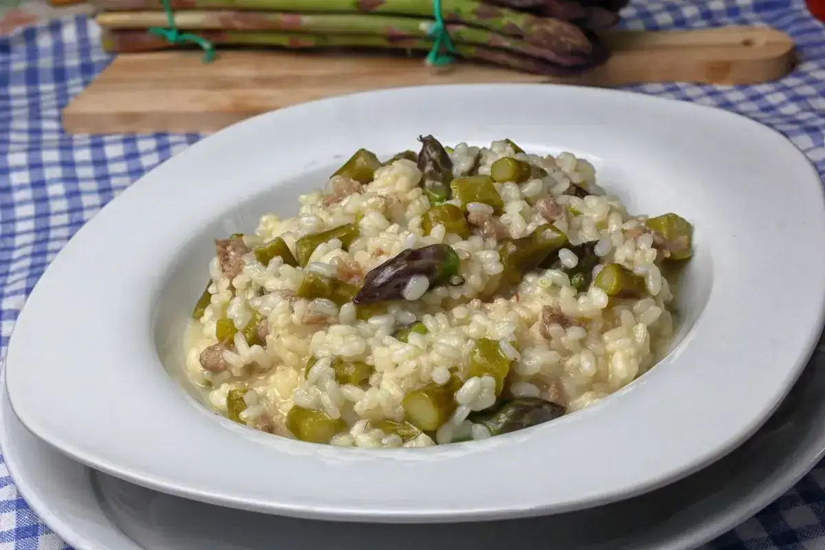 Un cremoso risotto asparagi e salsiccia, con asparagi freschi e pezzetti di salsiccia, servito in un piatto bianco.