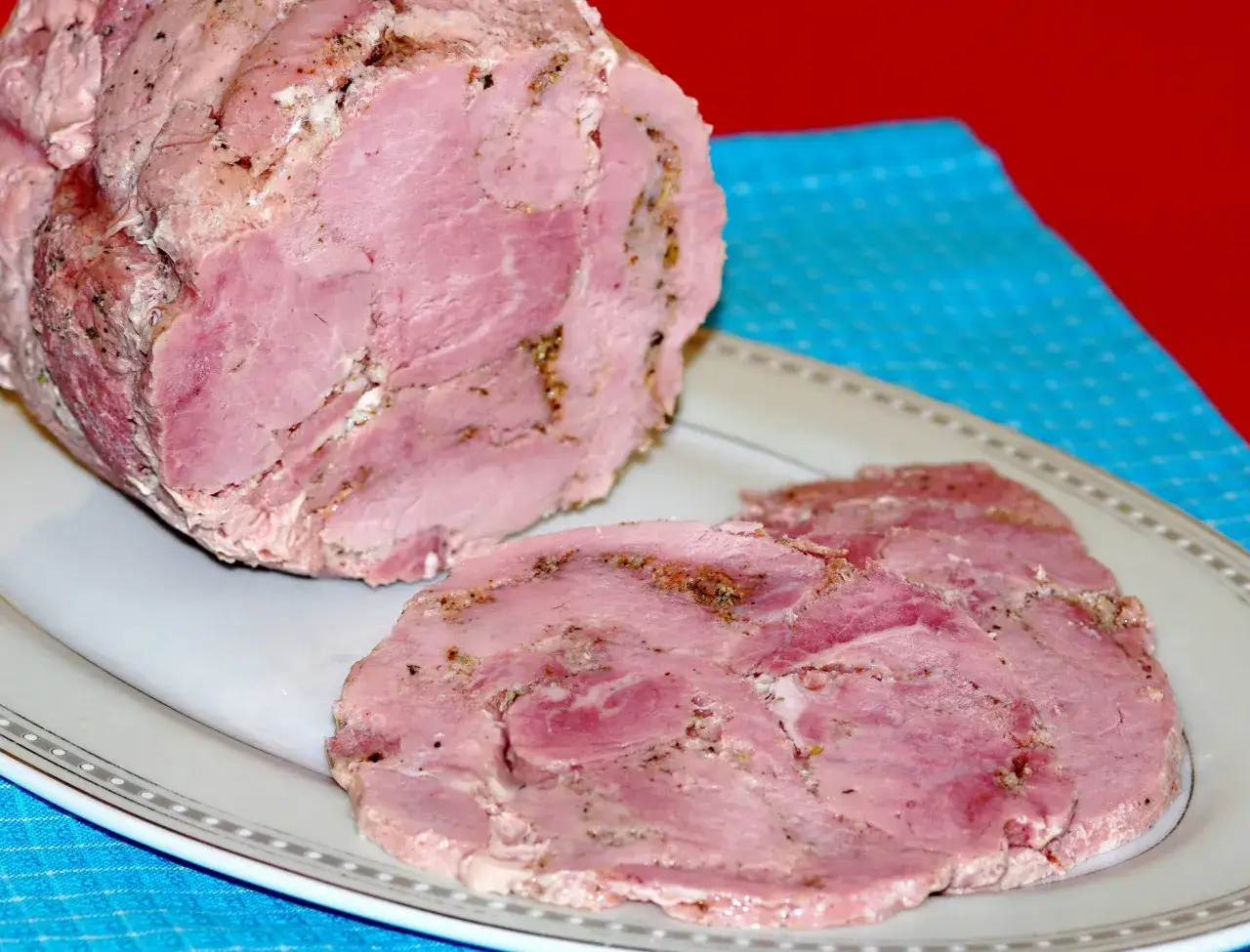 Pyszna, domowa szynka z szynkowara, pokrojona w plastry, prezentuje się apetycznie na talerzu.
