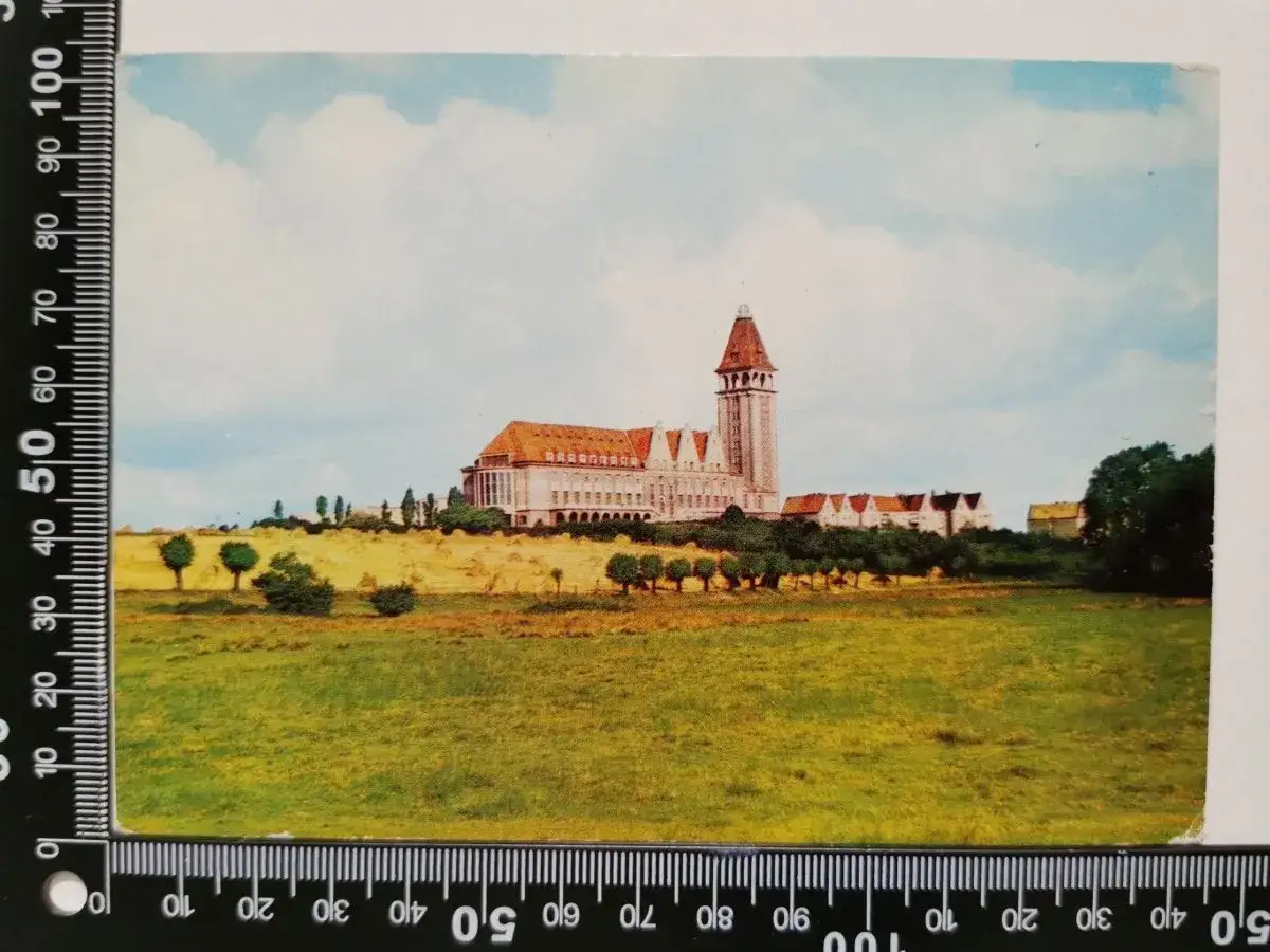 Imponujący budynek z wieżą, przypominający dawny dom rybaka, otoczony zielenią i polami.