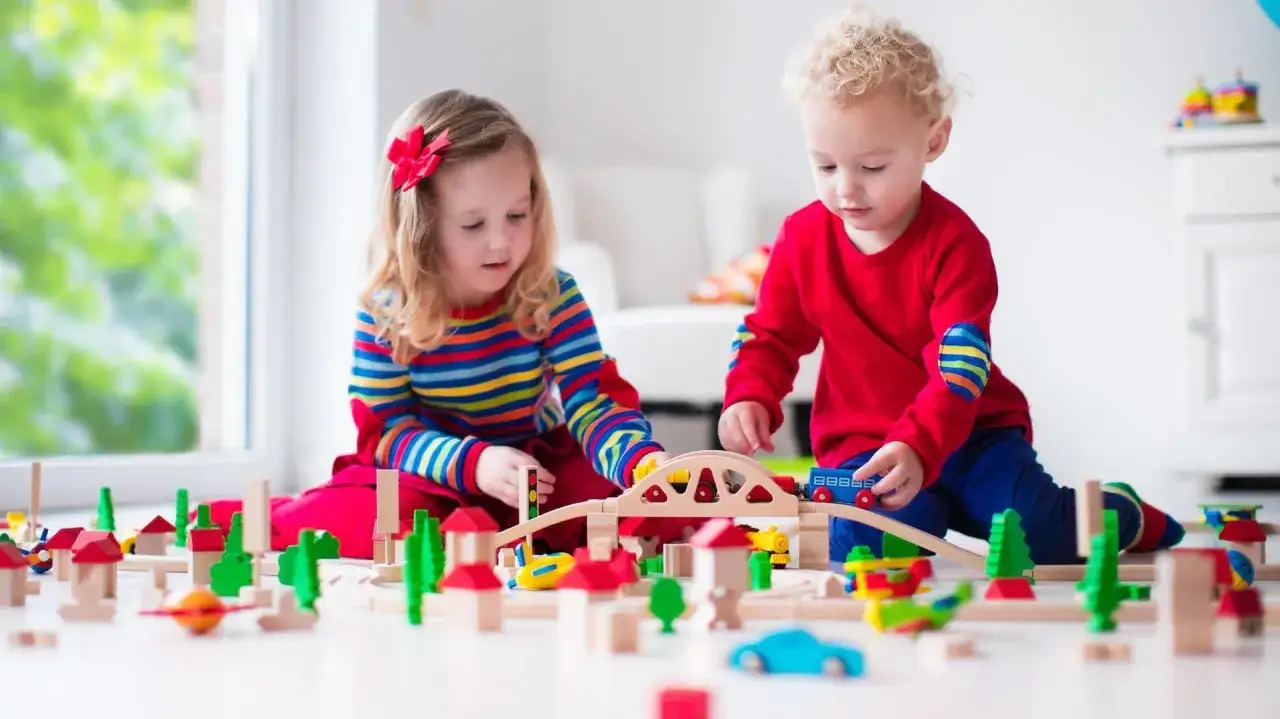 Zwei Kinder bauen eine Holzeisenbahn. Das Spielen fördert die Entwicklung, wie sie für die Kindergartenpflicht wichtig ist.