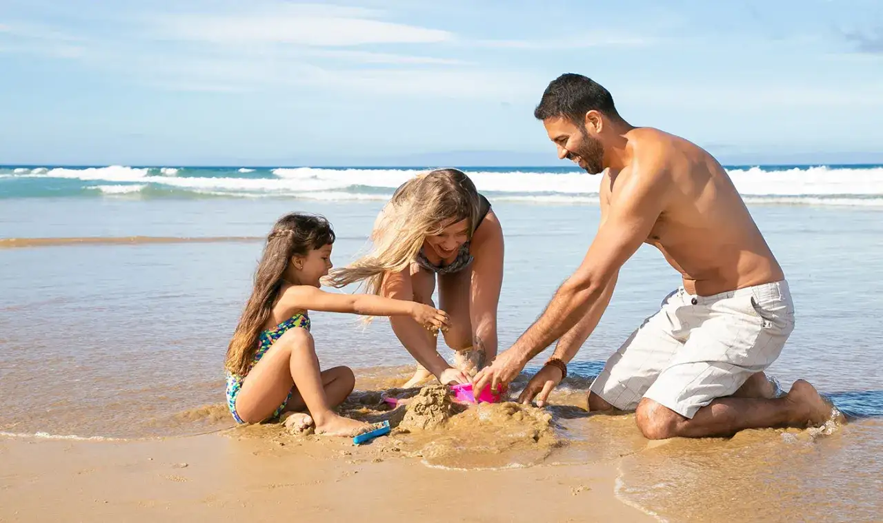 Familia construyendo un castillo de arena en las **playas de Valencia**. El sol brilla y las olas acarician la orilla.
