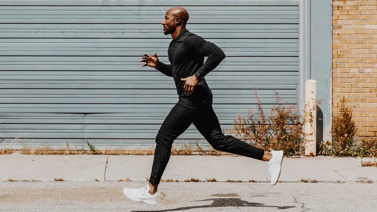 Ein Mann in schwarzer Sportkleidung macht slow jogging vor einer grauen Garagentür.