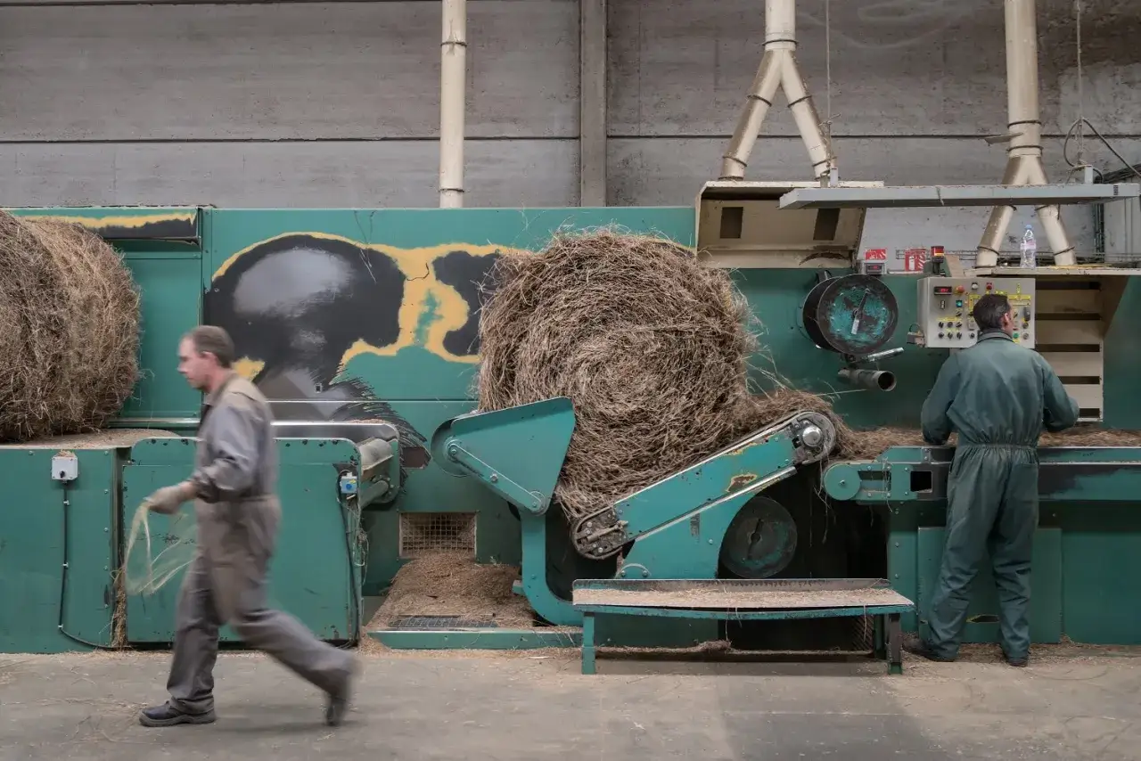 Dans une usine, des ouvriers supervisent la fabrication du lin, transformant de grosses balles de fibres v&eacute;g&eacute;tales en un processus industriel.