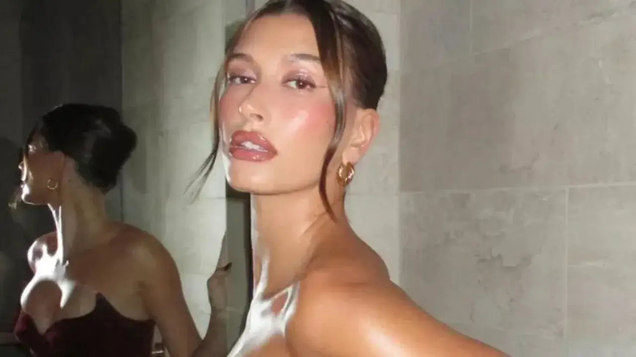 Hailey Bieber z lśniącą skórą, jak po użyciu ulubionego samoopalacza gwiazd. Jej odbicie w lustrze podkreśla efekt.