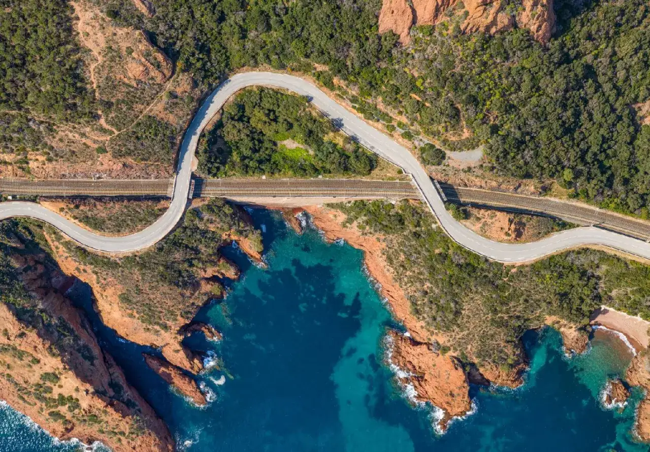 Strada tortuosa e ferrovia costeggiano la **corniche de l'Esterel**, tra rocce rosse e mare blu intenso.