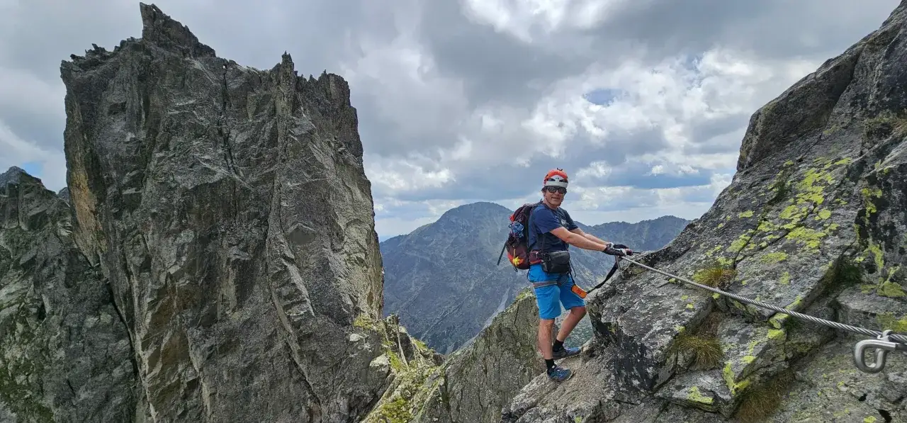 Mężczyzna na via ferrata polska, wspinający się po skalnej grani z widokiem na góry.
