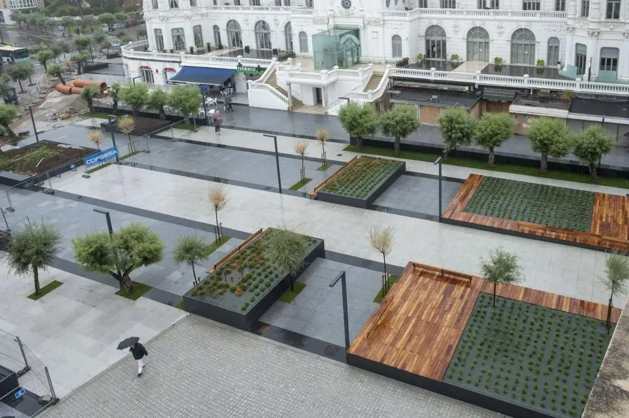 La **plaza Italia Santander** se muestra con jardineras elevadas, árboles y un edificio blanco al fondo.