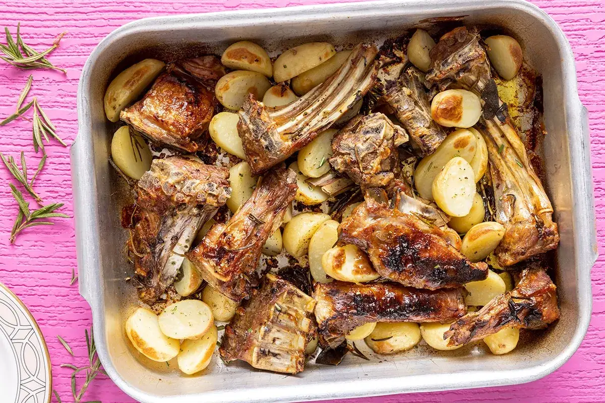 Abbacchio alla romana succulento e dorato, cotto al forno con patate e rosmarino in una teglia d'argento.
