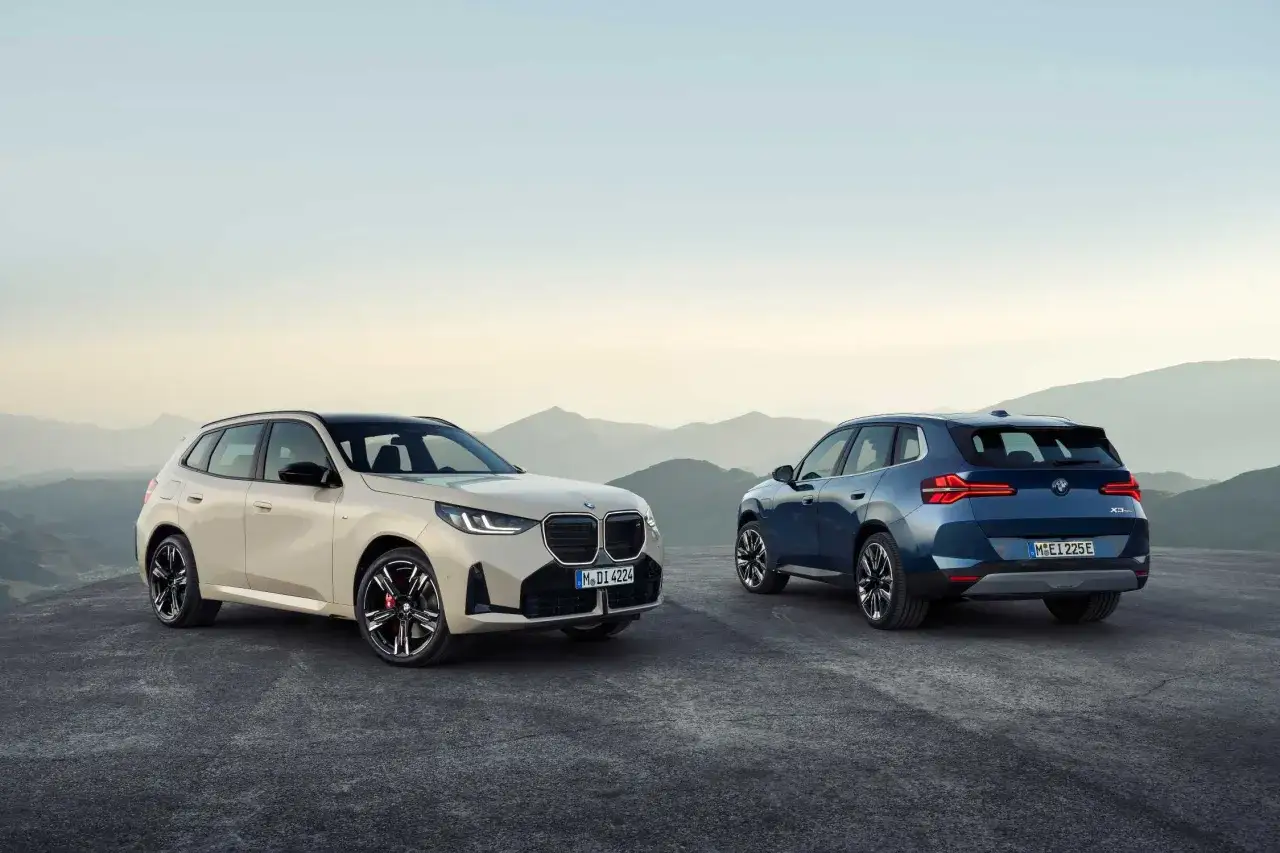 Dwa nowe BMW X3, jedno beżowe z przodu, drugie niebieskie z tyłu, stoją na tle gór.