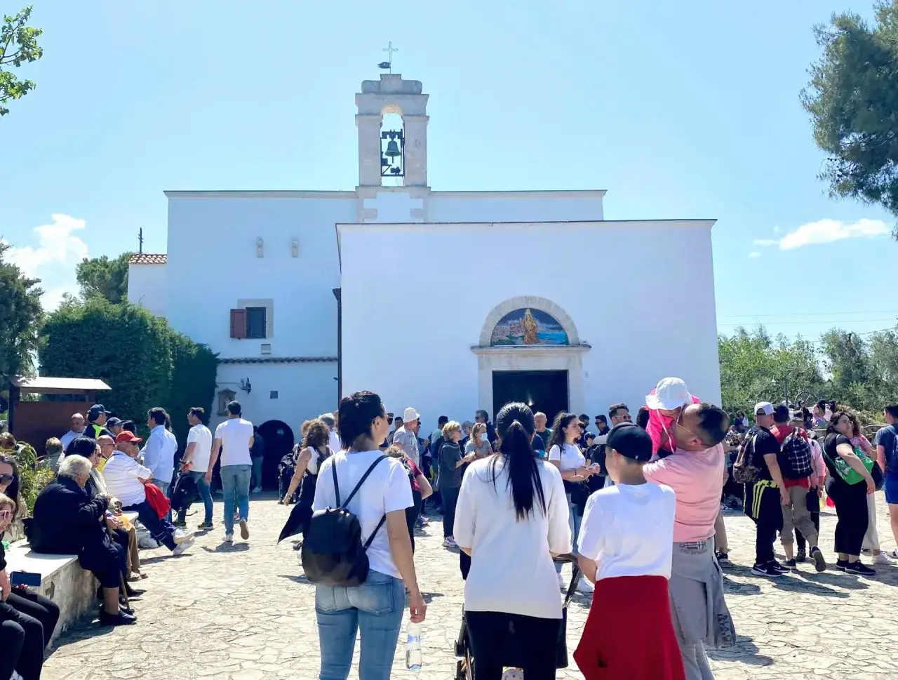 Folla di fedeli davanti alla chiesa di Santa Maria di Merino, con il campanile e un mosaico sopra l'arco d'ingresso.