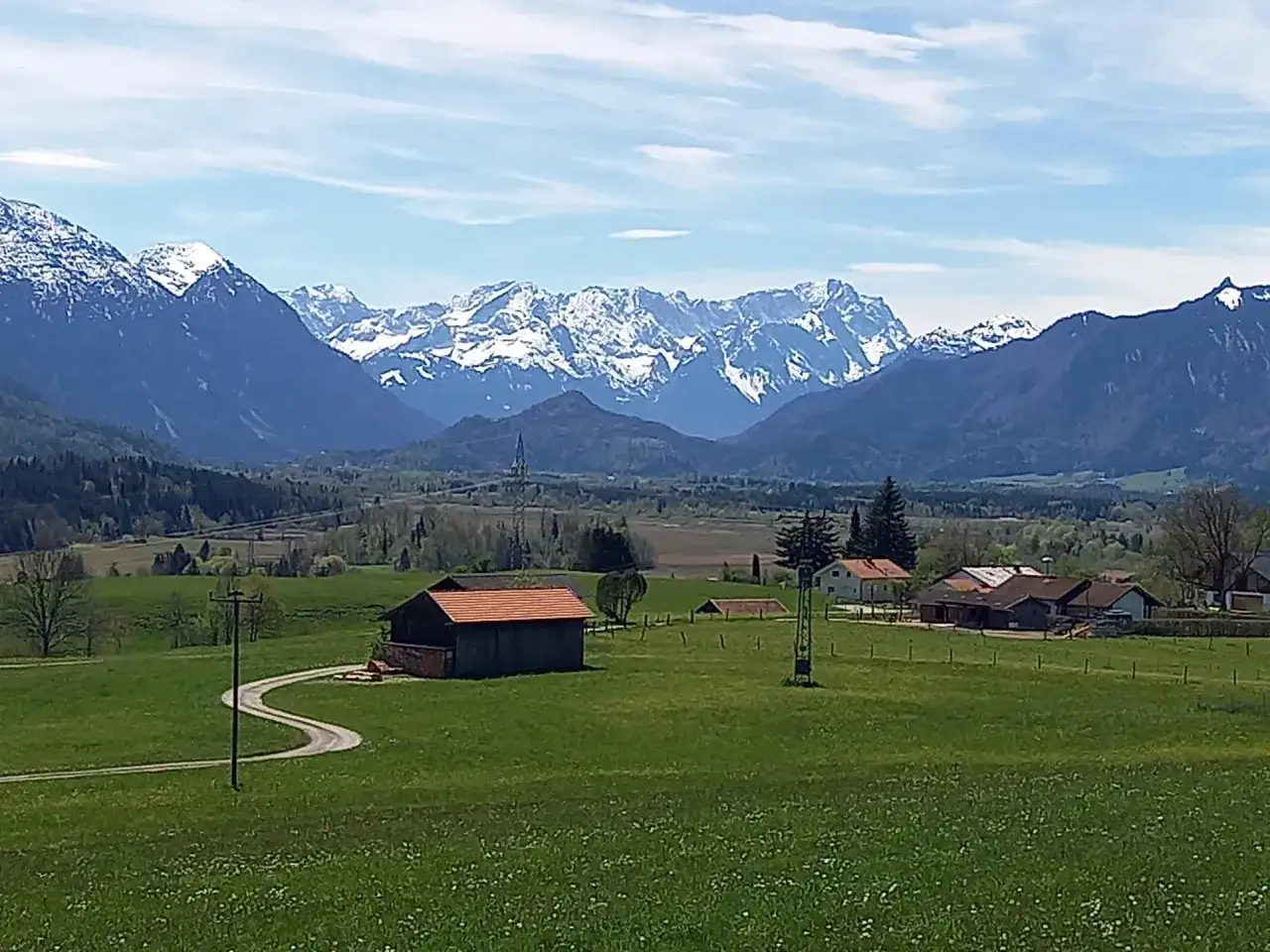 Idyllische Landschaft bei Murnau am Staffelsee mit schneebedeckten Bergen im Hintergrund, grünen Wiesen und einem Bauernhaus.