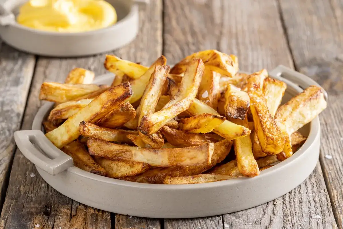 Patate in friggitrice ad aria, dorate e croccanti, servite in una ciotola su un tavolo di legno.