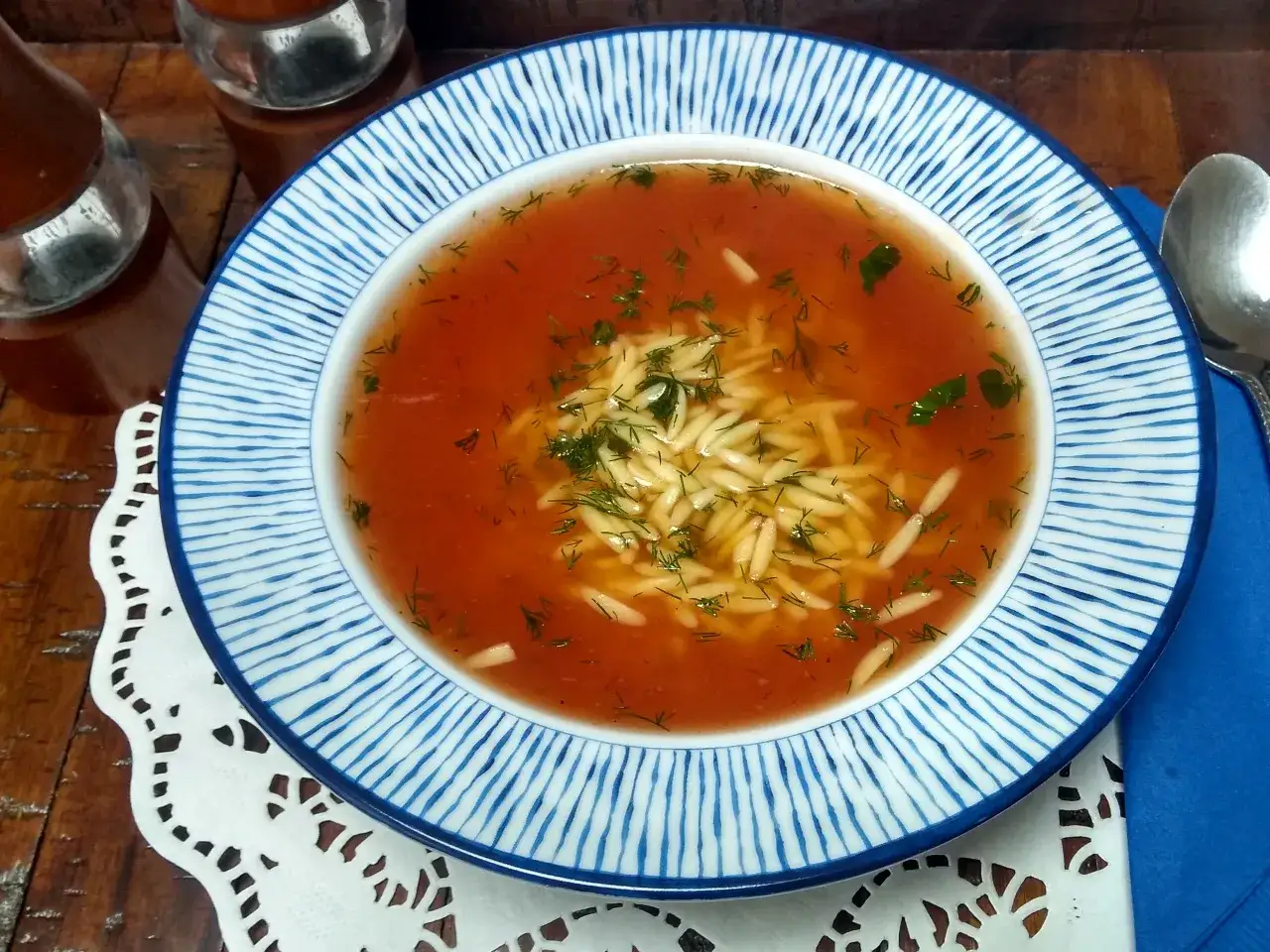Zupa pomidorowa z makaronem, ozdobiona koperkiem, na talerzu z niebieskimi paskami.